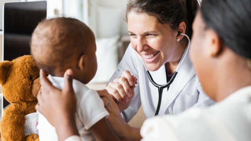 A doctor smiling while using a stethoscope on a baby, representing freedom to choose any provider without network restrictions.